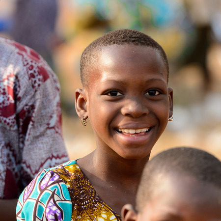 OUIDAH, BENIN - Jan 10, 2017: Unidentified Beninese girl with short hair smiles at the local market. Benin people suffer of poverty due to the bad economyのeditorial素材