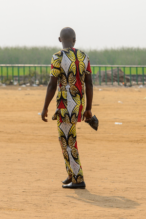 OUIDAH, BENIN - Jan 10, 2017: Unidentified Beninese man in colored suit walks on the street. Benin people suffer of poverty due to the bad economyのeditorial素材