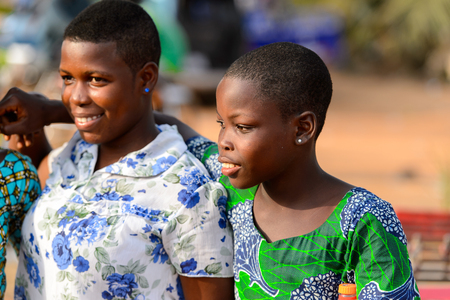 OUIDAH, BENIN - Jan 10, 2017: Unidentified Beninese girl in colored shirt hugs her friend at the local market. Benin people suffer of poverty due to the bad economyのeditorial素材
