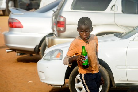 OUIDAH, BENIN - Jan 10, 2017: Unidentified Beninese little boy in dirty clothes holds a bottle in his hand at the local market. Benin children suffer of poverty due to the bad economyのeditorial素材