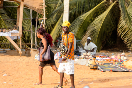 OUIDAH, BENIN - Jan 10, 2017: Unidentified Beninese man in colored clothes and funny yellow hat at the local market. Benin people suffer of poverty due to the bad economyのeditorial素材
