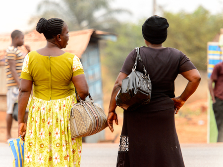 KUMASI, GHANA - Jan 16, 2017: Unidentified Ghanaian women in mustard and black dresses from behind. People of Ghana suffer of poverty due to the bad economyのeditorial素材