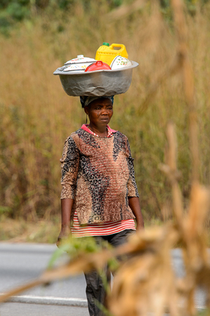 KUMASI, GHANA - Jan 16, 2017: Unidentified Ghanaian woman carries a basin on her head along the road . People of Ghana suffer of poverty due to the bad economyのeditorial素材