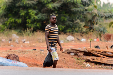 KUMASI, GHANA - Jan 16, 2017: Unidentified Ghanaian man  in striped shirt walks along the road with plastic bag. People of Ghana suffer of poverty due to the bad economyのeditorial素材