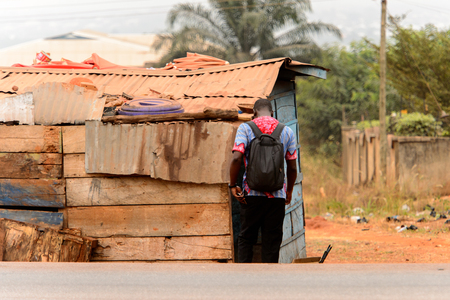 KUMASI, GHANA - Jan 16, 2017: Unidentified Ghanaian man with backpack from behind stands near the shack. People of Ghana suffer of poverty due to the bad economyのeditorial素材