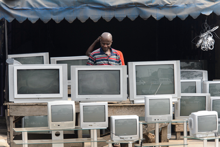 KUMASI, GHANA - Jan 16, 2017: Unidentified Ghanaian man in striped shirt stands behind TV sets. People of Ghana suffer of poverty due to the bad economyのeditorial素材