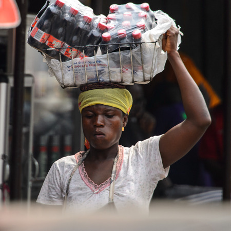 KUMASI, GHANA - Jan 16, 2017: Unidentified Ghanaian woman carries a basket with bottles of water on her head. People of Ghana suffer of poverty due to the bad economyのeditorial素材