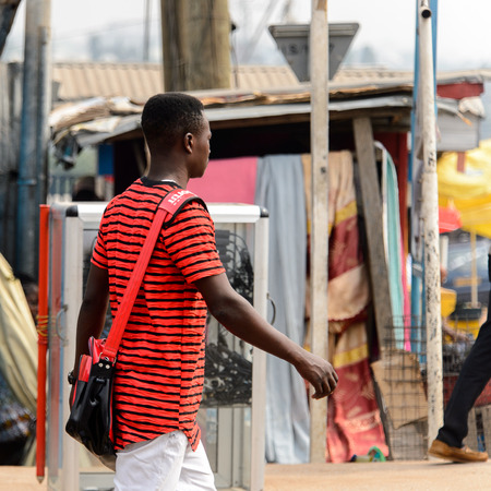 KUMASI, GHANA - Jan 16, 2017: Unidentified Ghanaian man in red striped shirt walks on the street. People of Ghana suffer of poverty due to the bad economyのeditorial素材