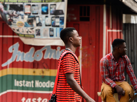 KUMASI, GHANA - Jan 16, 2017: Unidentified Ghanaian man in red striped shirt walks on the street. People of Ghana suffer of poverty due to the bad economyのeditorial素材