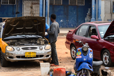 KUMASI, GHANA - Jan 16, 2017: Unidentified Ghanaian man in dark clothes from behind stands near the car with opened hood. People of Ghana suffer of poverty due to the bad economyのeditorial素材