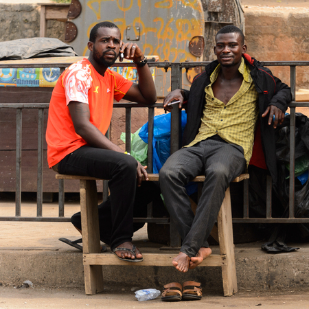 KUMASI, GHANA - Jan 16, 2017: Unidentified Ghanaian two men sit on the wooden bench. People of Ghana suffer of poverty due to the bad economyのeditorial素材