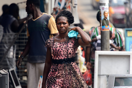 KUMASI, GHANA - Jan 16, 2017: Unidentified Ghanaian woman in beautiful dress with braids carries some clothes o her shoulder. People of Ghana suffer of poverty due to the bad economyのeditorial素材