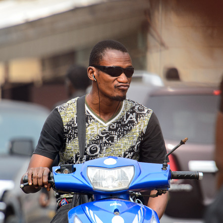 KUMASI, GHANA - Jan 16, 2017: Unidentified Ghanaian man in sunglasses and headphones rides a motorcycle. People of Ghana suffer of poverty due to the bad economyのeditorial素材
