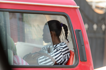 CENTRAL REGION, GHANA - Jan 17, 2017: Unidentified Ghanaian woman looks out of the red car's window in local village. People of Ghana suffer of poverty due to the bad economyのeditorial素材