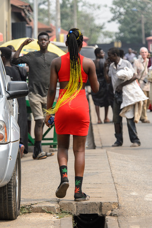 KUMASI, GHANA - Jan 16, 2017: Unidentified Ghanaian stylish woman with braids in red dress walks on the street. People of Ghana suffer of poverty due to the bad economyのeditorial素材