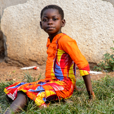 KUMASI, GHANA - Jan 16, 2017: Unidentified Ghanaian little boy in colored clothes sits on the grass. Childrenof Ghana suffer of poverty due to the bad economyのeditorial素材