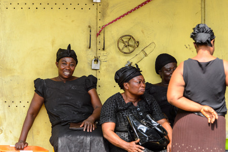 KUMASI, GHANA - Jan 16, 2017: Unidentified Ghanaian women in black clothes sit near the gate. People of Ghana suffer of poverty due to the bad economyのeditorial素材