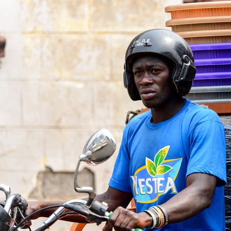 KUMASI, GHANA - Jan 16, 2017: Unidentified Ghanaian man in helmet and blue shirt rides a motorcycle. People of Ghana suffer of poverty due to the bad economyのeditorial素材