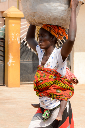 CENTRAL REGION, GHANA - Jan 17, 2017: Unidentified Ghanaian woman carries a baby and a basin on her head in local village. People of Ghana suffer of poverty due to the bad economyのeditorial素材