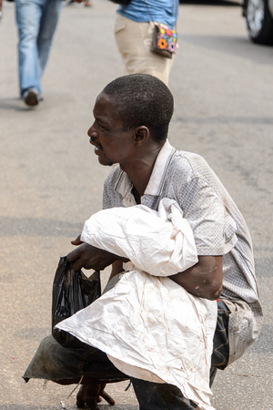 KUMASI, GHANA - Jan 16, 2017: Unidentified Ghanaian man holds plastic bag on squats. People of Ghana suffer of poverty due to the bad economyのeditorial素材