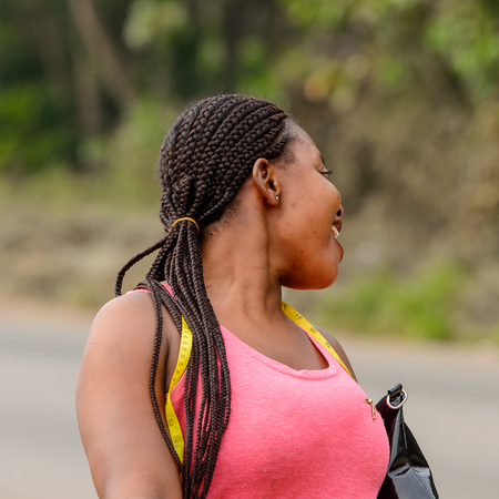 CENTRAL REGION, GHANA - Jan 17, 2017: Unidentified Ghanaian woman in pink shirt with braids smiles in local village. People of Ghana suffer of poverty due to the bad economyのeditorial素材
