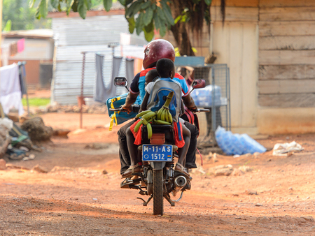 KUMASI, GHANA - Jan 16, 2017: Unidentified Ghanaian man in helmet rides a motorcycle with couple of kids behind. People of Ghana suffer of poverty due to the bad economyのeditorial素材