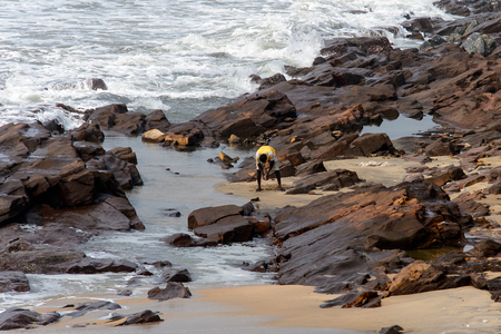 ELMINA, GHANA -JAN 18, 2017: Unidentified  Ghanaian man bends down for something on the coast of Elmina. People of Ghana suffer of poverty due to the bad economyのeditorial素材