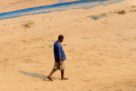 ELMINA, GHANA -JAN 18, 2017: Unidentified  Ghanaian man in blue shirt walks on the coast of Elmina with fishing net on background. People of Ghana suffer of poverty due to the bad economyのeditorial素材