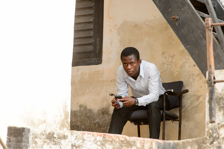 ELMINA, GHANA -JAN 18, 2017: Unidentified  Ghanaian man sits on a chair with a cellphone in his hands. People of Ghana suffer of poverty due to the bad economyのeditorial素材