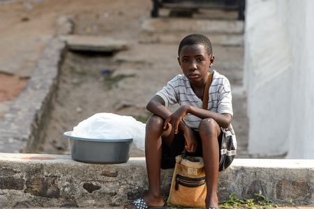 ELMINA, GHANA -JAN 18, 2017: Unidentified  Ghanaian little boy sits on the foundation next to the basin in Elmina. Children of Ghana suffer of poverty due to the bad economyのeditorial素材