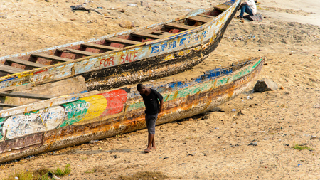 ELMINA, GHANA -JAN 18, 2017: Unidentified  Ghanaian man hangs out near canoes on the coast of Elmina. People of Ghana suffer of poverty due to the bad economyのeditorial素材
