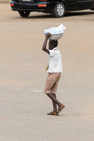 ELMINA, GHANA -JAN 18, 2017: Unidentified  Ghanaian man from behind walks with a basin on his head in Elmina. People of Ghana suffer of poverty due to the bad economyのeditorial素材