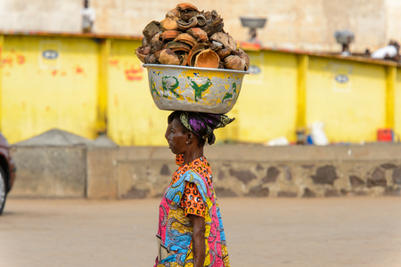 ELMINA, GHANA -JAN 18, 2017: Unidentified  Ghanaian woman in colored dress carries a basin on her head in Elmina. People of Ghana suffer of poverty due to the bad economyのeditorial素材