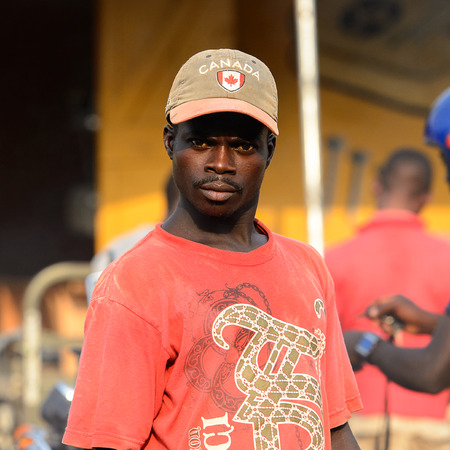 CENTRAL REGION, GHANA - Jan 17, 2017: Unidentified Ghanaian man in red shirt and a cap looks ahead in local village. People of Ghana suffer of poverty due to the bad economyのeditorial素材