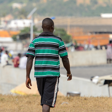 ELMINA, GHANA -JAN 18, 2017: Unidentified  Ghanaian man from behind walks in striped shirt on the coast of Elmina. People of Ghana suffer of poverty due to the bad economyのeditorial素材