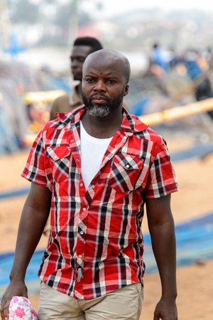 ELMINA, GHANA -JAN 18, 2017: Unidentified  Ghanaian man in plaid shirt walks along the coast of Elmina. People of Ghana suffer of poverty due to the bad economyのeditorial素材