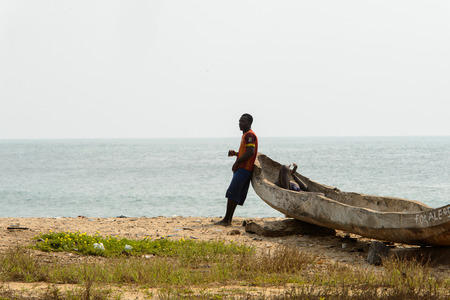 ELMINA, GHANA -JAN 18, 2017: Unidentified  Ghanaian man stands near the broken boat on the coast of Elmina. People of Ghana suffer of poverty due to the bad economyのeditorial素材