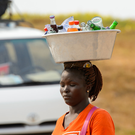 ELMINA, GHANA -JAN 18, 2017: Unidentified  Ghanaian woman carries a basin with bottles on her head in Elmina. People of Ghana suffer of poverty due to the bad economyのeditorial素材