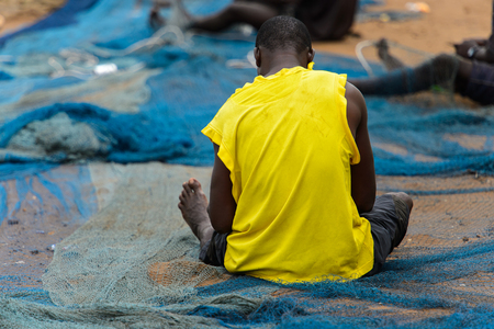 ELMINA, GHANA -JAN 18, 2017: Unidentified  Ghanaian man weaves a fishing net on the coast of Elmina. People of Ghana suffer of poverty due to the bad economyのeditorial素材