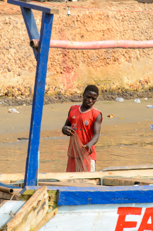 ELMINA, GHANA -JAN 18, 2017: Unidentified  Ghanaian man in red shirt holds a fishing net in Elmina port. People of Ghana suffer of poverty due to the bad economyのeditorial素材