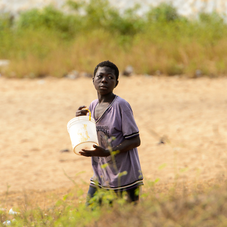ELMINA, GHANA -JAN 18, 2017: Unidentified  Ghanaian boy carries a bucket on the coast of Elmina. People of Ghana suffer of poverty due to the bad economyのeditorial素材