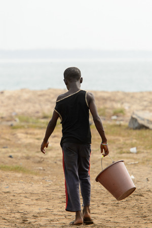 ELMINA, GHANA -JAN 18, 2017: Unidentified  Ghanaian little boy walks on the coast of Elmina with a bucket. Children of Ghana suffer of poverty due to the bad economyのeditorial素材