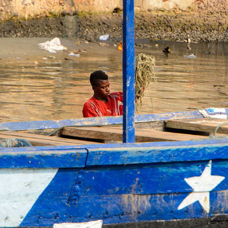 ELMINA, GHANA -JAN 18, 2017: Unidentified  Ghanaian man in red shirt holds a fishing net in Elmina port. People of Ghana suffer of poverty due to the bad economyのeditorial素材