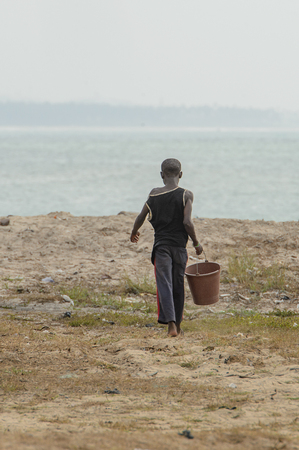 ELMINA, GHANA -JAN 18, 2017: Unidentified  Ghanaian little boy walks on the coast of Elmina with a bucket. Children of Ghana suffer of poverty due to the bad economyのeditorial素材