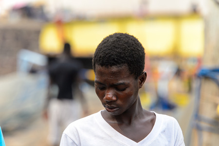 ELMINA, GHANA -JAN 18, 2017: Unidentified  Ghanaian boy in white shirt looks down in Elmina port. People of Ghana suffer of poverty due to the bad economyのeditorial素材