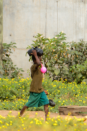 ELMINA, GHANA -JAN 18, 2017: Unidentified  Ghanaian boy blows a baloon and carries a plastic bag on his head in Elmina. Children of Ghana suffer of poverty due to the bad economyのeditorial素材