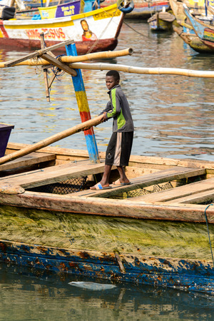 ELMINA, GHANA -JAN 18, 2017: Unidentified  Ghanaian boy stands in the boat on the coast of Elmina. People of Ghana suffer of poverty due to the bad economyのeditorial素材