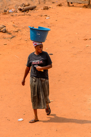 ELMINA, GHANA -JAN 18, 2017: Unidentified  Ghanaian woman carries a basin on her head on the coast of Elmina. People of Ghana suffer of poverty due to the bad economyのeditorial素材