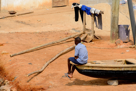 ELMINA, GHANA -JAN 18, 2017: Unidentified  Ghanaian boy sits on the boat on the shore of Elmina port. People of Ghana suffer of poverty due to the bad economyのeditorial素材