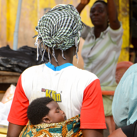 ELMINA, GHANA -JAN 18, 2017: Unidentified  Ghanaian woman carries a baby on her back in Elmina....